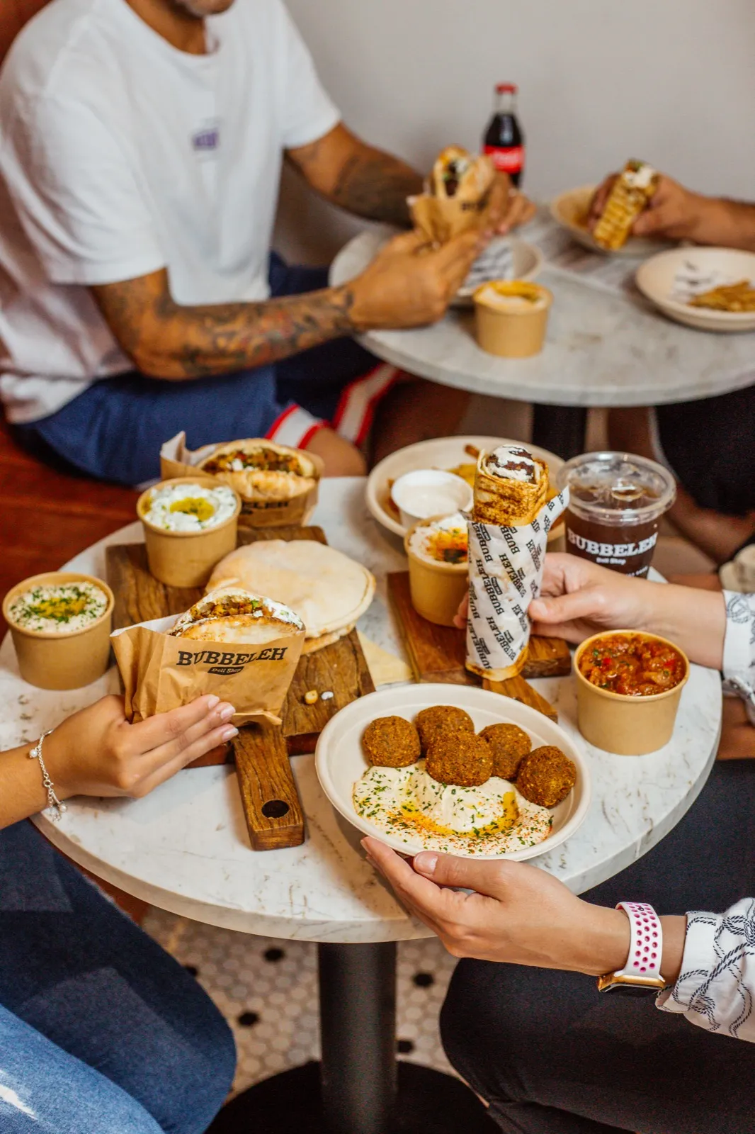 Mesa do Bubbeleh em Pinheiros com falafel, homus, pita e pessoas compartilhando