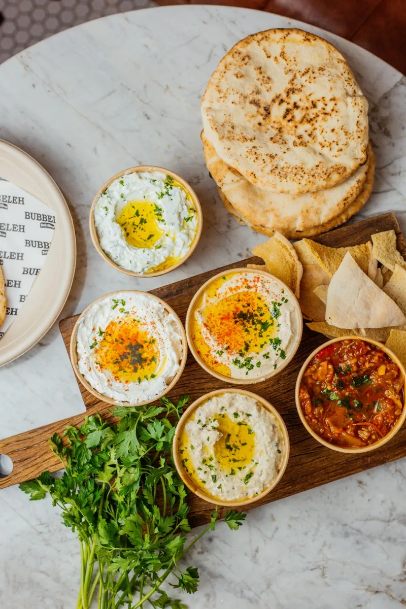 Mesa vegana mediterrânea no Bubbeleh em Pinheiros: homus, babaganush, matbuha e pão pita