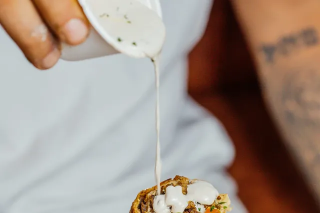 Tahine cremosa sendo despejada sobre a shawarma do Bubbeleh, um dos molhos feitos do zero na casa